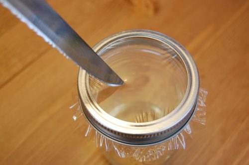 בעזרת סכין, צרו חורים בניילון נצמד המכסה את צוואר הצנצנת.