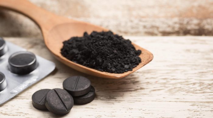 טבליות שלמות של פחם פעיל על השולחן וטבליות מרוסקות בכפית