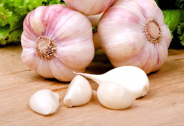 ישנם שלושה ראשי שום וארבע שיני שום על שולחן עץ.