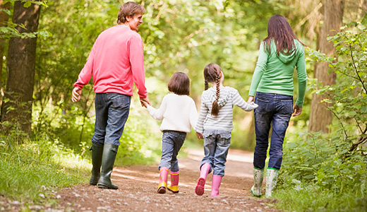 אב בסוודר ורוד, אם בז'קט ירוק ושתי בנות בטיול בפארק, נראות מאחור
